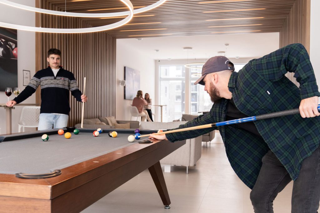 Résidents jouant au billard dans la salle commune du complexe condo Quartier 7 illustrant la vie communautaire